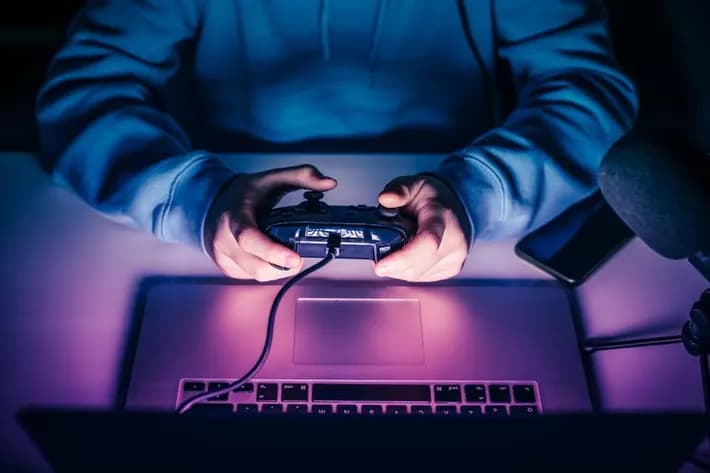 A person holding a game controller in front of a laptop